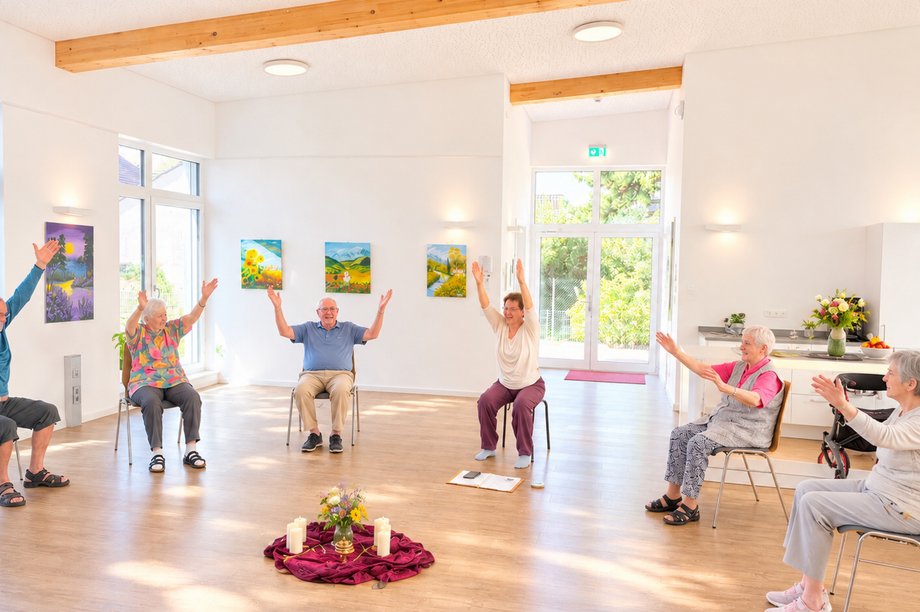 Bewohnerinnen und Bewohner nehmen an einer Yoga-Einheit im AWO-Seniorenzentrum am Feldrain teil und führen Übungen im Sitzen aus.
