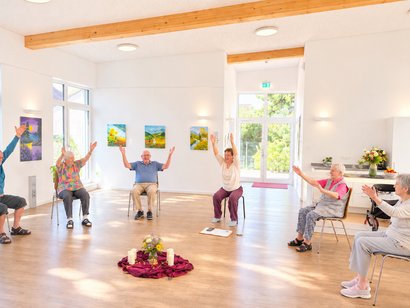 Bewohnerinnen und Bewohner nehmen an einer Yoga-Einheit im AWO-Seniorenzentrum am Feldrain teil und führen Übungen im Sitzen aus.