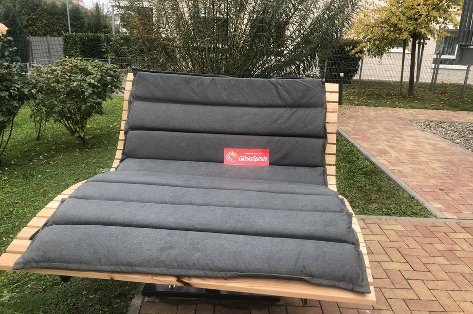 Barrierefreie Doppelliege im Gartenbereich eines Seniorenzentrums, gefördert durch die GlücksSpirale, umgeben von Grünflächen und Wegen.